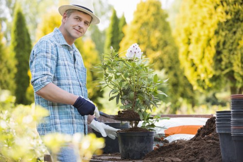 Operative wearing PPE including gloves, boots and hi-vis performing gardening work